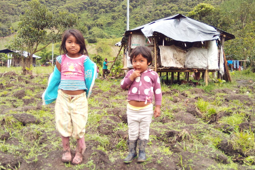 Zwei kleine Mädchen stehen in schmutziger Kleidung auf einem Feld. Im Hintergrund ist eine Holzhütte