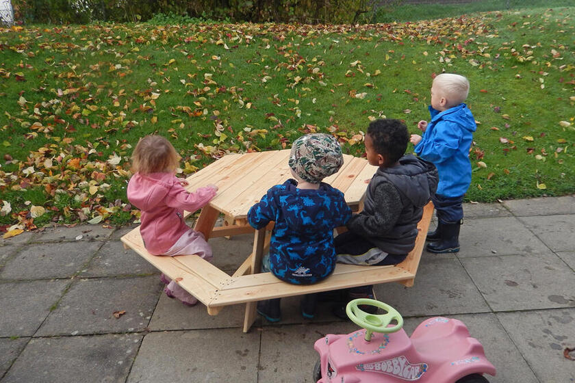 Vier Kinder sitzen an einer Kinderbank mit Tisch