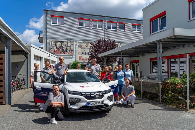 Auf dem Foto ist das Team des Ambulanten Pflegedienstes Lübeck zu sehen, die sich um ein Dienstauto gruppiert haben.