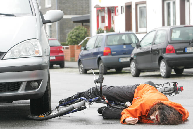 ein Radfahrer liegt verletzt und am Kopf blutend auf der Straße, neben einem Auto