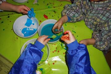 Kinderhände tauchen Papier in blaue Farbe.