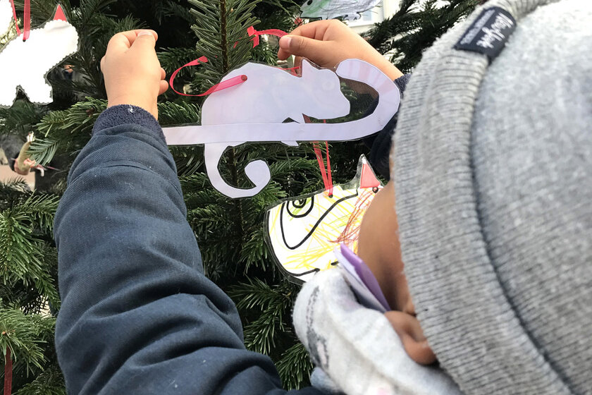 Kita-Kind schmückt den Tannenbaum mit einem Chamäleon-Anhänger. 