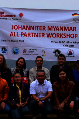 Participants of the workshop in Myanmar stand in front of the Johanniter logo.