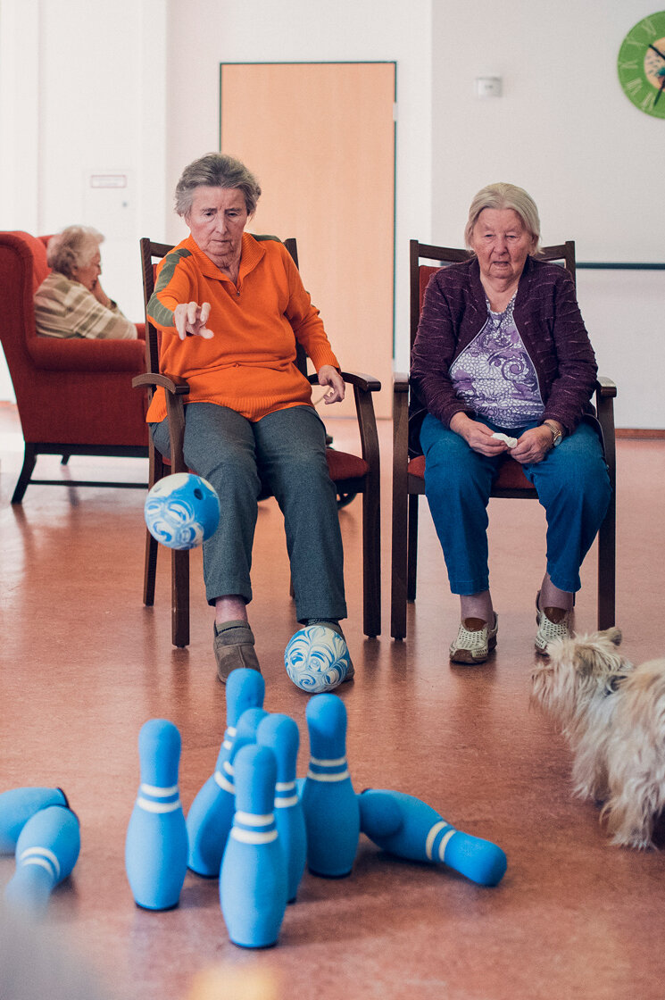 Zwei Seniorinnen kegeln im Sitzen auf dem Flur im Johanniter-Quartier Lübeck
