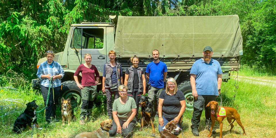 Hundeführerinnen und Hundeführer mit ihren Tieren vor einem alten Armeefahrzeug