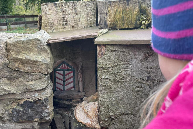 Ein Kind schaut auf eine kleine Koboldtür im Wald