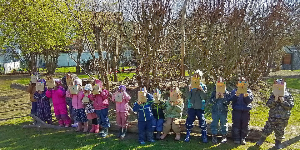Kinder im Außengelände der Kita mit Ostertüten, die wie Hasen aussehen