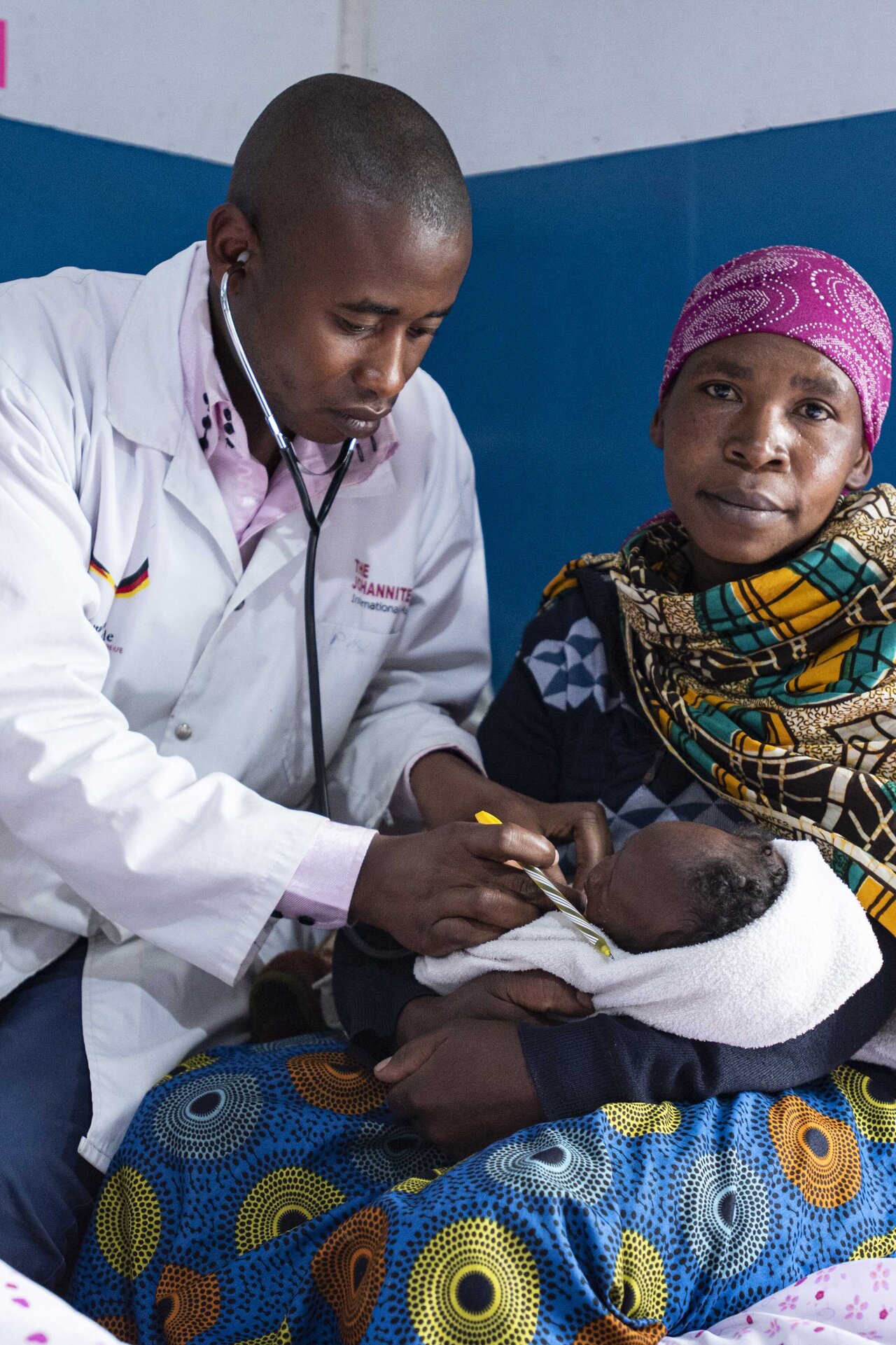 Ein Baby wird auf dem Schoß seine Mutter von einem Arzt untersucht