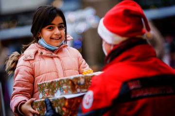 Eine Johanniterin mit Weihnachtsmütze übergibt einem strahlenden Kind ein Geschenk