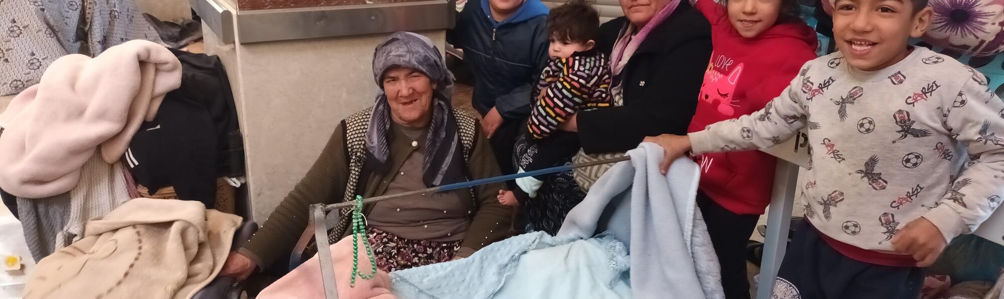 Zwei Frauen mit Kopftuch sitzen mit mehreren Kindern in einer Notunterkunft.
