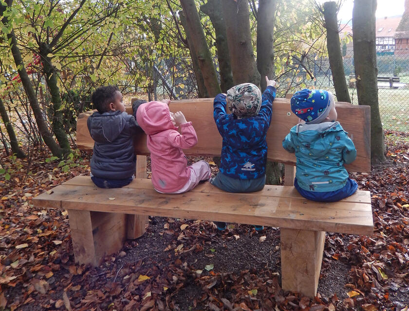 Vier Kinder sitzen auf einer Bank und schauen in die Natur