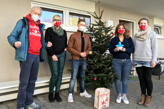 5 Personen stehen draußen am Weihnachtsbaum mit einer Weihnachtstüte