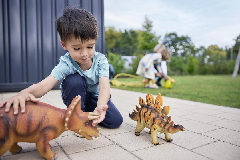 Auf dem Bild ist ein Junge zu sehen, der mit Dinosauriern spielt.
