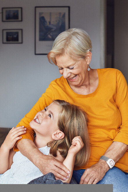 Eine Großmutter mit ihrer Enkelin. Die Oma trägt einen Hausnotruf-Sender am Handgelenk.