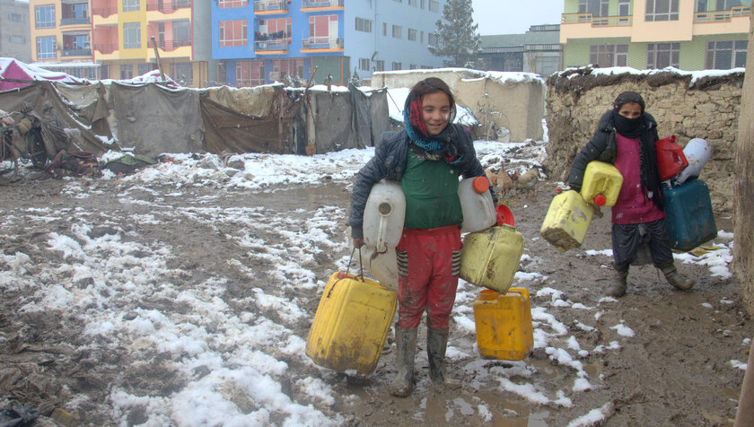 Kinder tragen die leeren Wasserbehälter zur Wasserstelle.