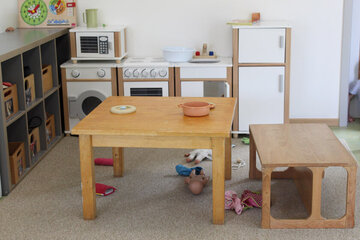 Im Hintergrund sieht man eine Kinder-Spielküche, davor ist ein kleiner Tisch mit Stühlen. 