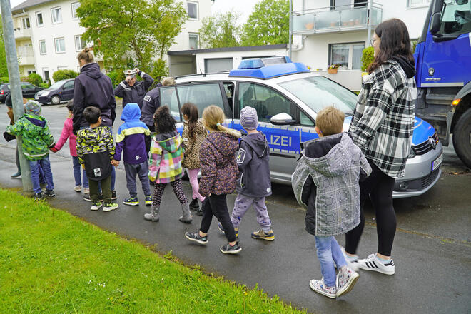 Kinder gehen neben einem Polizeiwagen auf einem Weg entlang