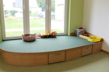 Erhöhung mit grünem Teppich auf der die Kinder mit Bauklötzen bauen und mit anderen Spielsachen spielen können.