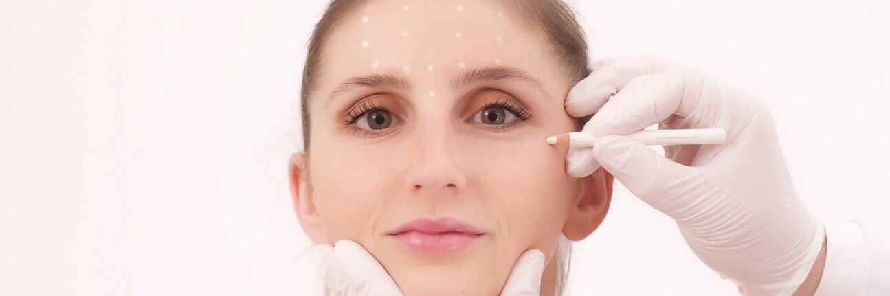 Gesicht einer Frau welches mit einem weißen Stift punktuell markiert wird für Ihren Eingriff