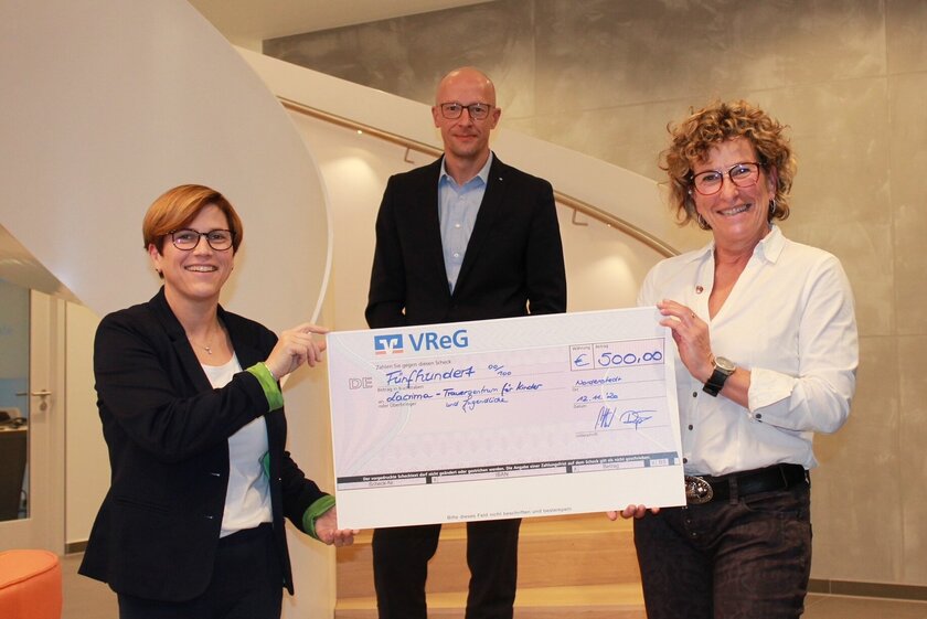 Jens-Hartwig Göttsch (Bereichsleiter VReG Region Norderstedt) und Kathleen Röpke (Mitarbeiterin Marketing VReG) überreichen der ehrenamtlichen Johanniterin Bettina Schröder den Spendenscheck.