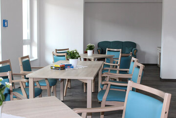 Blick in den Gemeinschaftsraum mit seinen Tischen und gemütlichen blauen Stühlen. 