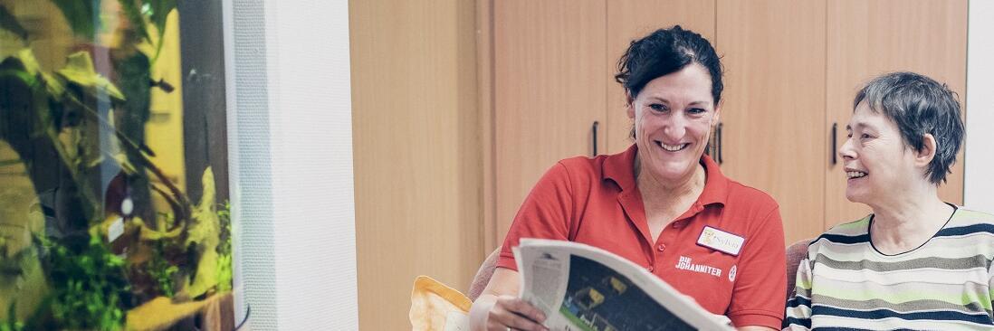 Eine Mitarbeiterin liest mit einer Bewohnerin eine Zeitung