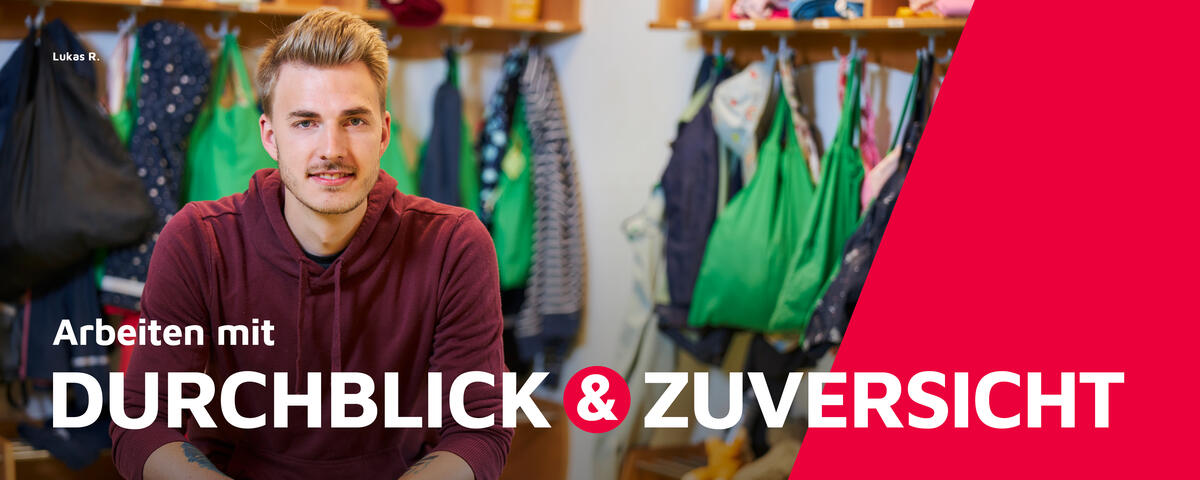 Ein Mitarbeiter der Johanniter sitzt vor einer Garderobe.