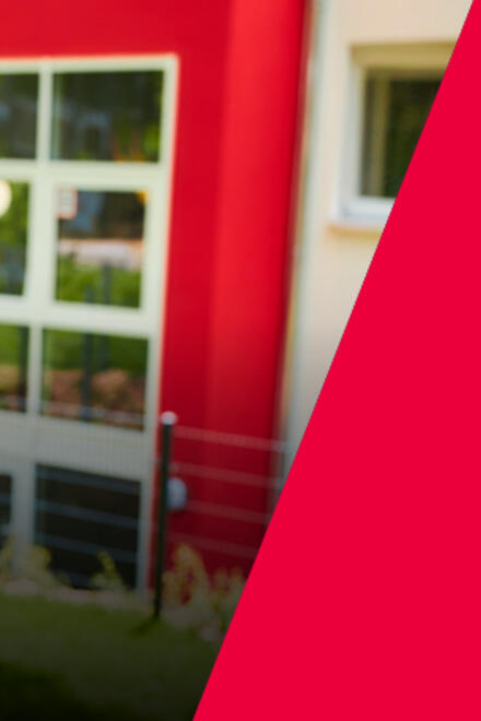 Eine Mitarbeiterin der Johanniter steht vor einem Gebäude im Grünen.